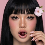 Woman with a flower in her hair holding a cherry against a pink background
