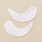 Two lotus patterned undereye patches on a creamy beige background.