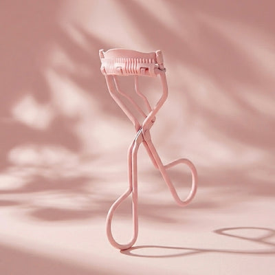 Pink eyelash curler on a soft pink background